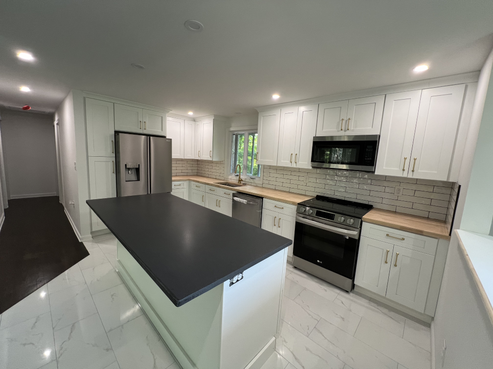 Modern kitchen with white cabinets, dark countertop, stainless steel appliances, and subway tile backsplash, featuring natural light from windows.