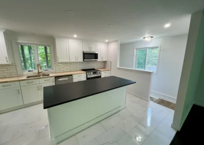 Modern kitchen featuring white cabinetry, black countertop island, stainless steel appliances, and large windows overlooking greenery