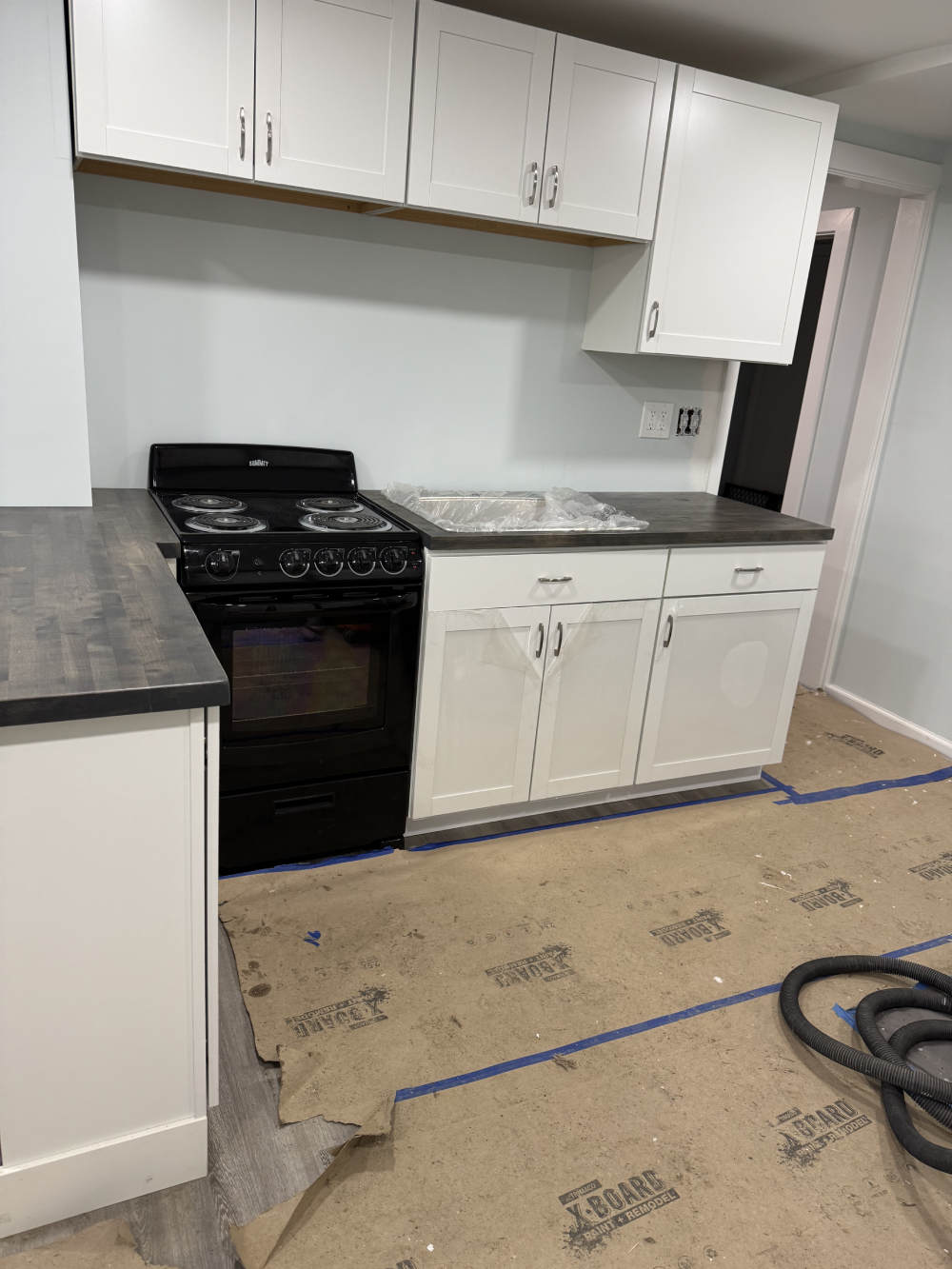 Newly remodeled kitchen with black stove, white cabinets, and a countertop. Floor covered with protective paper, indicating ongoing renovation Newly remodeled kitchen with black stove, white cabinets, and a countertop. Floor covered with protective paper, indicating ongoing renovation