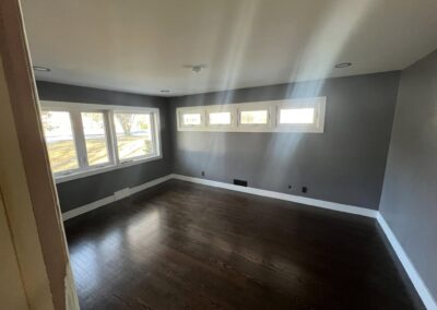 Freshly added room with dark hardwood flooring, smooth gray walls, and bright white trim. Features a row of large windows on one wall and smaller rectangular transom windows on another, allowing natural light to fill the space. Located in Windsor, Connecticut.