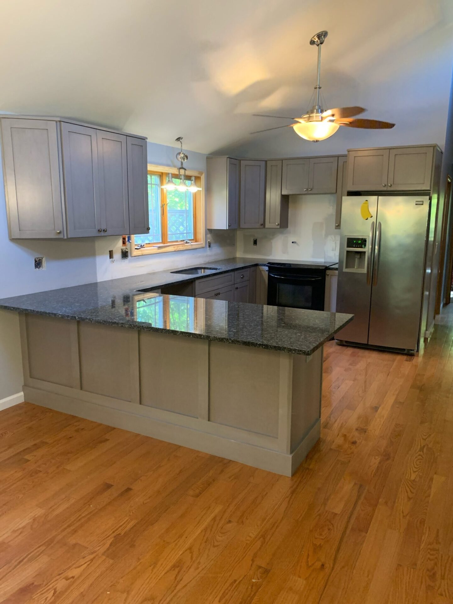 Modern kitchen in a newly built in-law suite addition in Vernon, CT, featuring granite countertops, wood flooring, and gray shaker cabinets.