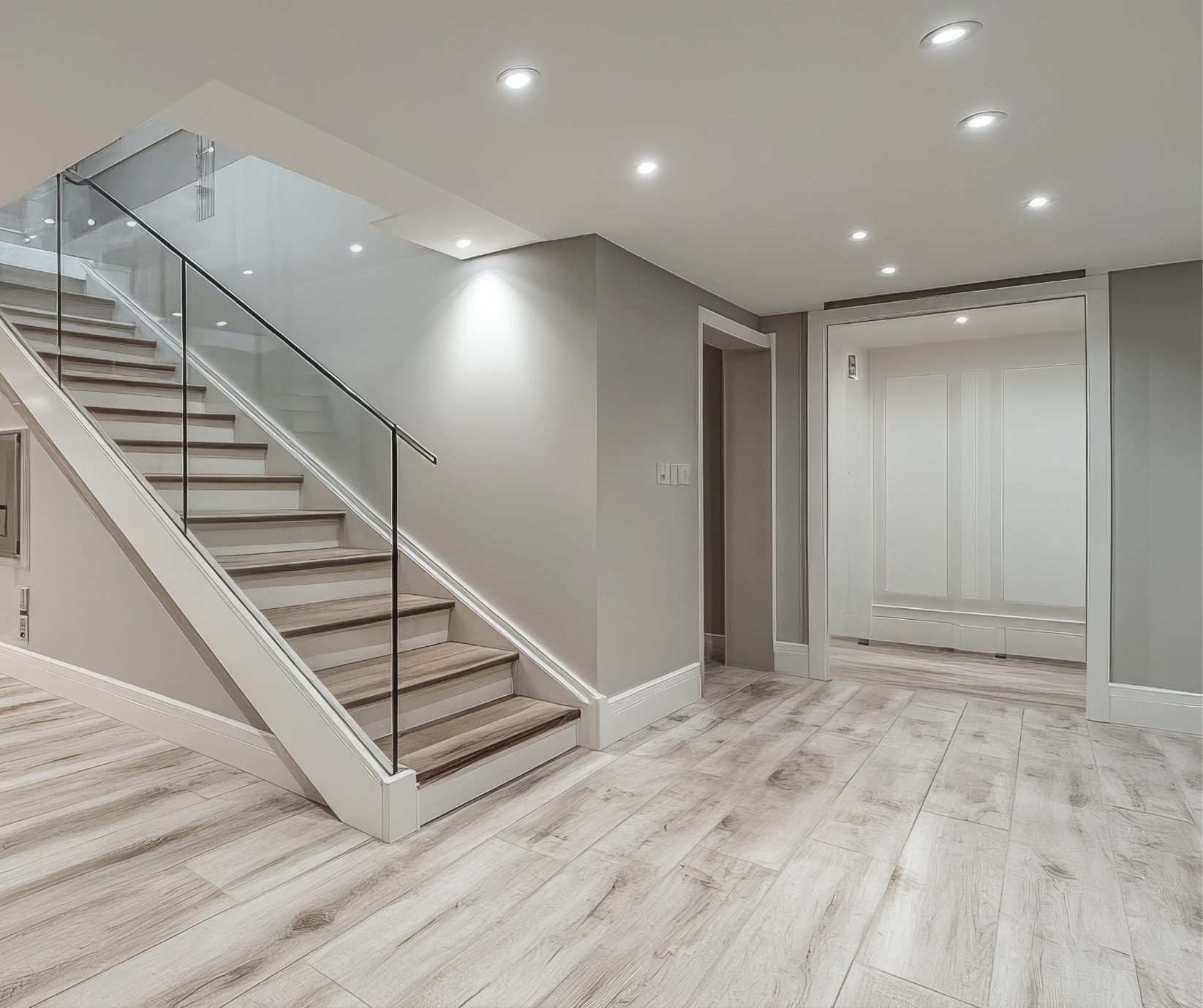 Basement finish in Andover, CT Basement finishing in Tolland County CT with light wood-look tile flooring, recessed lights, and glass stair railing